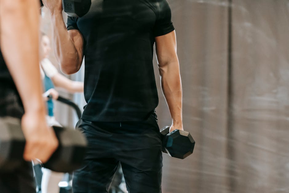 Muscular male pumping biceps with heavy metal dumbbells near mirror during workout