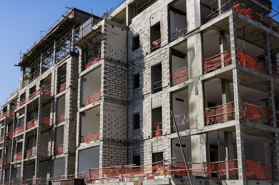 A modern multi-story apartment building under construction with scaffolding and safety netting